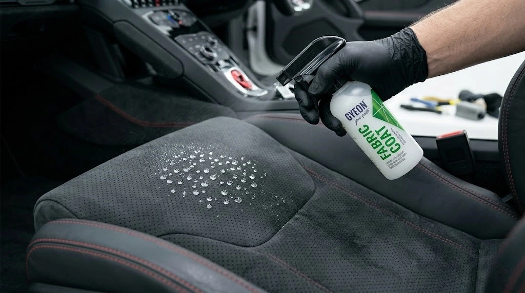 Gyeon FabricCoat sprej i kapljice vode na zaštićenom crnom alcantara sedištu automobila — efekat hidrofobnosti