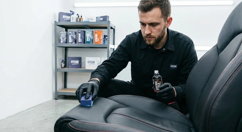 Gyeon tehničar nanosi LeatherShield keramičku zaštitu aplikatorom na crno kožno sedište automobila sa crvenim šavovima