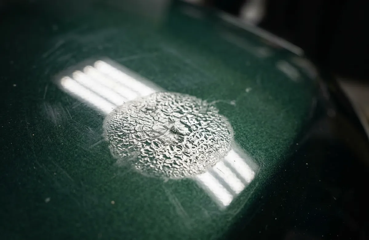 Kavitacija laka nastala od zapeklog ptičijeg izmeta ili smole na zelenom automobilu — hemijsko oštećenje koje poliranje ne može sanirati