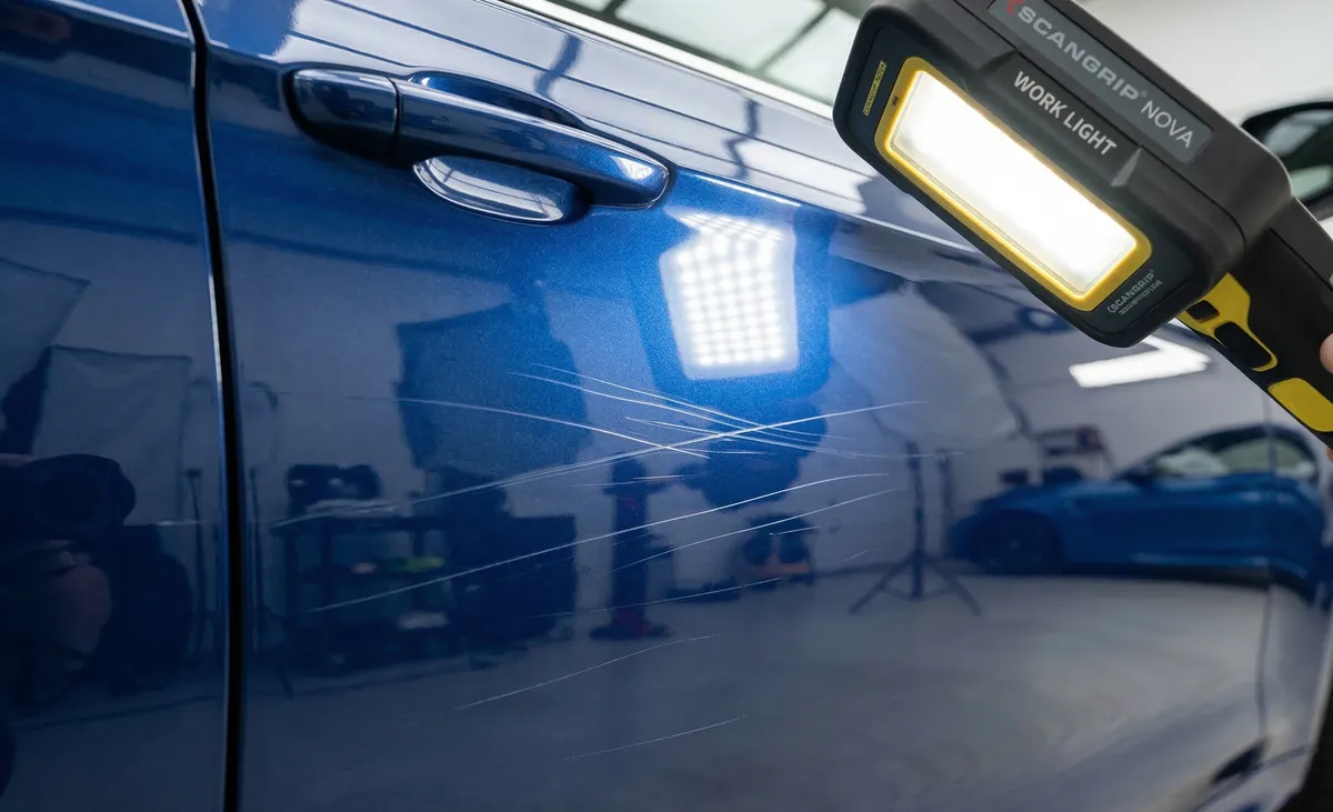 Srednje duboke ogrebotine od granja na plavom laku automobila otkrivene Scangrip work light lampom u detailing studiju